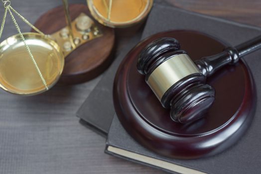 Wood gavel, soundblock, scales and stack of old books bound in leather on the wooden background