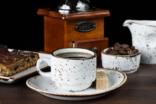 Vintage ceramic cup of coffee, coffee beans, coffee mill, cane sugar and a piece of chocolate cake