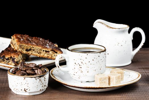 Vintage ceramic cup of coffee, coffee beans, cane sugar and a piece of chocolate cake