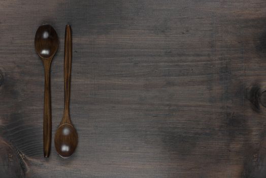 Wooden spoons lie on a dark wooden background with copy-space