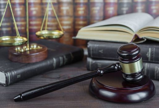 Wood gavel, soundblock, scales and open old book against the background of a row of antique books bound in leather