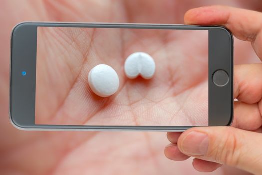 Two white pills in palm of white man. Medical product. Take medicine. Tablets on smartphone screen.