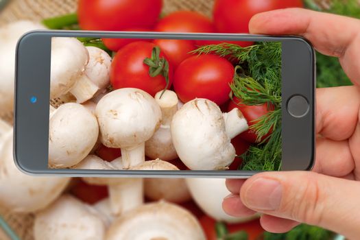 Fresh vegetables. Ingredients for cooking. Tomatoes and champignons on the smartphone screen.