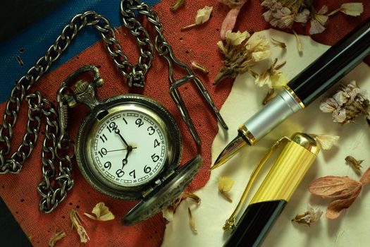 Vintage pocket watch and brass pen on old book. At 8 o'clock in morning. Closeup and Top view. Education and vintage style concept.