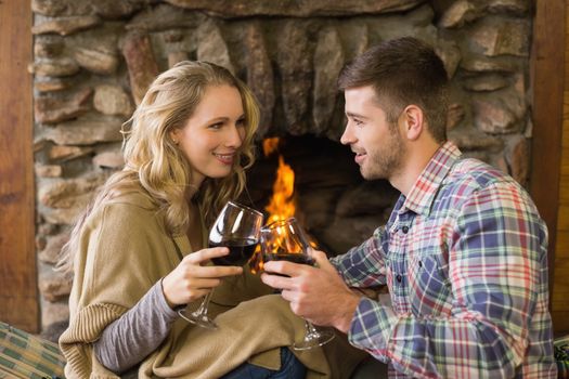 Romantic young couple toasting wineglasses in front of lit fireplace