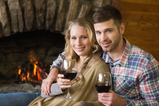 Portrait of a romantic young couple with wineglasses in front of lit fireplace