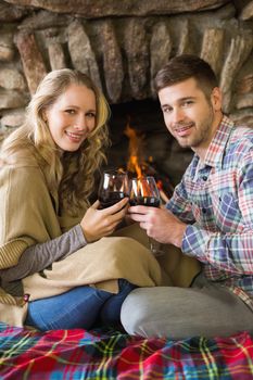 Side view portrait of a romantic young couple toasting wineglasses in front of lit fireplace