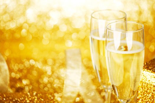 Champagne in glasses and gift box on golden background with twinkle lights