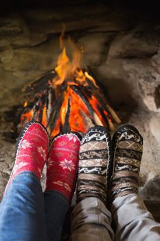 Close up of romantic couples legs in socks in front of fireplace at winter season at home