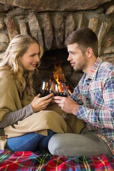 Side view of a romantic young couple toasting wineglasses in front of lit fireplace