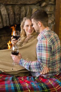 Romantic young couple with wineglasses looking at each other in front of lit fireplace