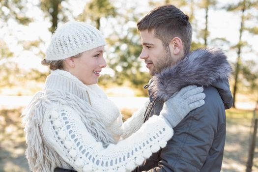 Side view of a loving young couple looking at each other in winter clothing in the woods