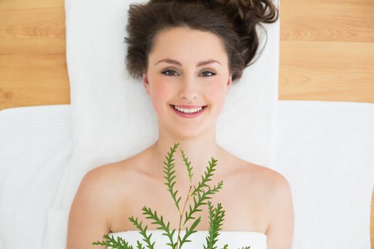 Overhead portrait of a young brunette lying with leaves on massage table in beauty salon