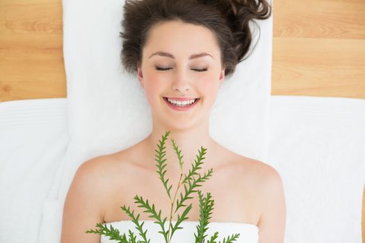 Overhead view of a young brunette lying with leaves on massage table in beauty salon