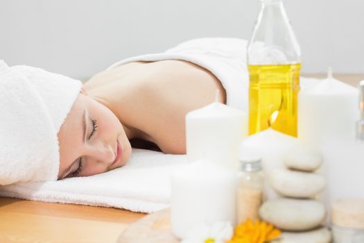 Beautiful young woman resting with oil bottle in foreground at beauty spa
