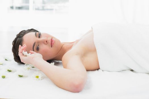 Portrait of a beautiful young woman with flowers lying in beauty salon