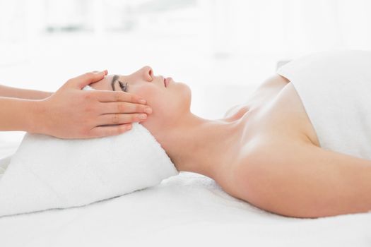 Side view of hands massaging a beautiful womans face at beauty spa