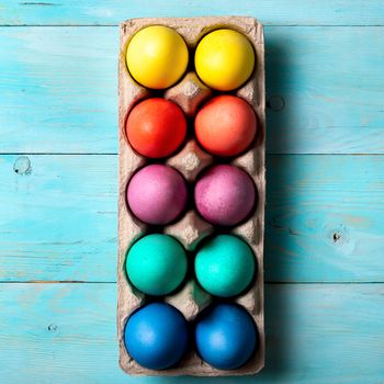 Easter concept. Colorful eggs in cardboard packaging on blue wooden background. Top down view or flat lay. Square shape