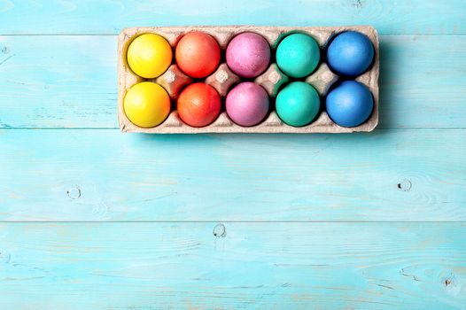 Easter concept. Colorful eggs in cardboard packaging on blue wooden background with copy space for text. Top down view or flat lay