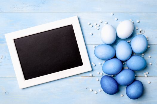 Easter concept. Ombre eggs in blue colors on blue wooden background with empty chalkboard. Top down view or flat lay. Classic blue colors in Easter 2020. Copy space for text