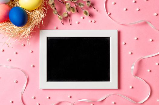 Orthodox Easter concept. Colorful eggs and pussy willow branches on pink background with empty chalkboard. Copy space for greetings, text or design. Top down view or flat lay