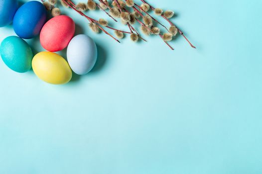 Orthodox Easter concept. Colorful eggs and pussy willow branches on blue background with empty chalkboard. Copy space for greetings, text or design. Top down view or flat lay