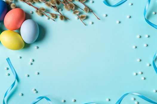 Orthodox Easter concept. Colorful eggs and pussy willow branches on blue background with empty chalkboard. Copy space for greetings, text or design. Top down view or flat lay