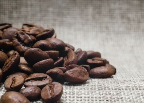 heap of roasted coffee beans on a matting macro beige background closeup
