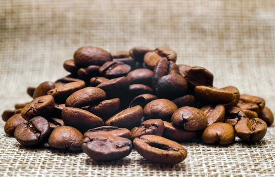 heap of coffee beans on a matting macro beige background closeup