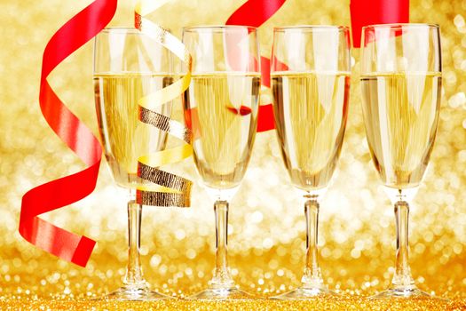 Glasses of champagne and red ribbons on golden background