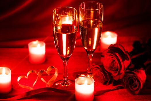 Valentines day celebration, glasses of champagne, candles, roses and hearts on red silk