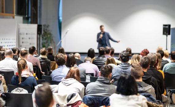 Speaker giving a talk in conference hall at business event. Audience at the conference hall. Business and Entrepreneurship concept. Focus on unrecognizable people in audience.