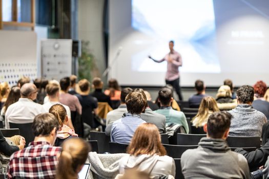 Speaker giving a talk in conference hall at business event. Rear view of unrecognizable people in audience at the conference hall. Business and entrepreneurship concept.