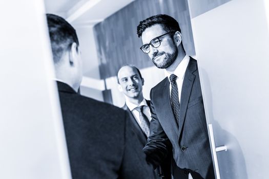 Group of confident business people greeting with a handshake at business meeting in modern office. Closing the deal agreement by shaking hands. Greyscale blue toned image.