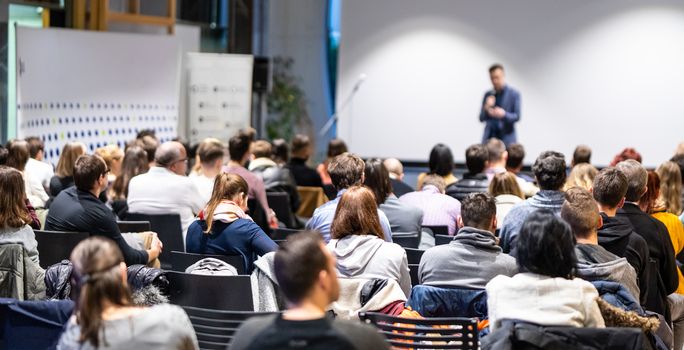 Speaker giving a talk in conference hall at business event. Rear view of unrecognizable people in audience at the conference hall. Business and entrepreneurship concept.