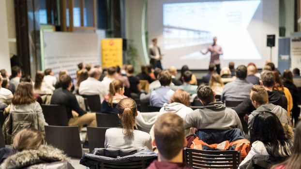 Speaker giving a talk in conference hall at business event. Rear view of unrecognizable people in audience at the conference hall. Business and entrepreneurship concept.