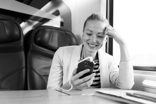 Caucasian businesswoman communicating on cellphone using headphone set while traveling by train in business class seat. Black and white photo.