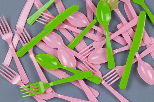 Background from reusable recyclable pink and green forks, spoons, knifes made from corn starch on grey paper. Eco, zero waste, alternative to plastic concept. Flat lay, top view. Horizontal. Closeup.