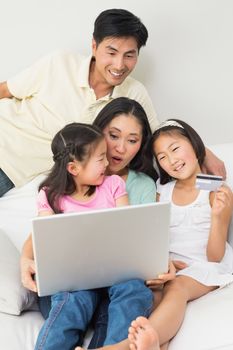 Happy family of four doing online shopping through laptop and credit card at home
