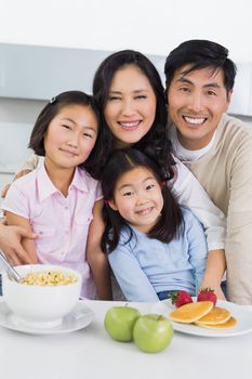 Portrait of a smiling couple with happy two daughters having breakfast in the kitchen at home