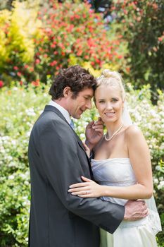 Romantic smiling newlyweds embracing looking at camera in the countryside