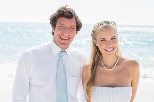 Romantic couple smiling at camera on their wedding day at the beach