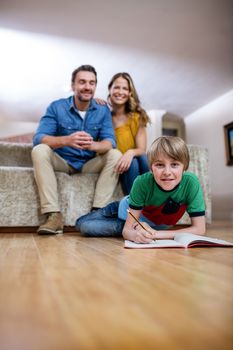 Boy doing homework while parents sitting on sofa in background at home