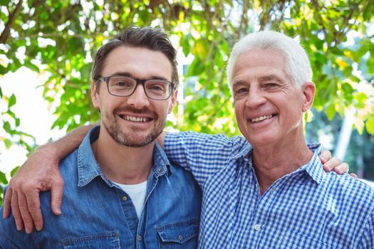 Portrait of happy father and son with arm around while standing outdoors
