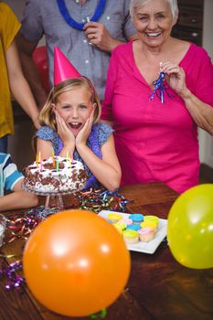Portrait of shocked girl with family celebrating birthday at home