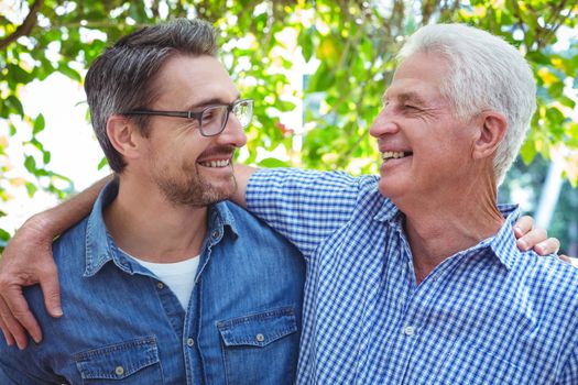 Cheerful father and son with arm around while standing outdoors