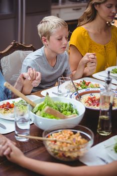 Family holding hands while praying at dining table in home