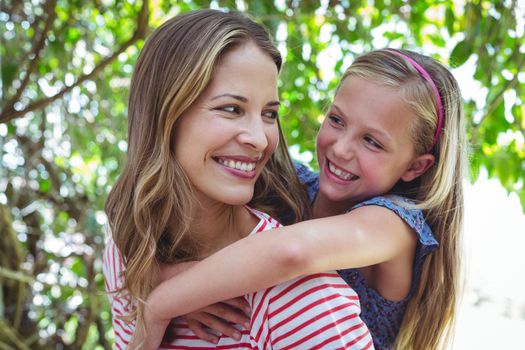 Happy mother giving piggy-back to daughter while standing outdoors