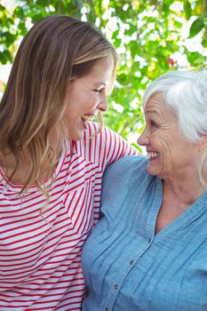 Cheerful mother and daughter with arm around while standing outdoors