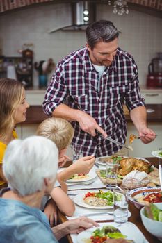 Father serving food while standing at dining table with family